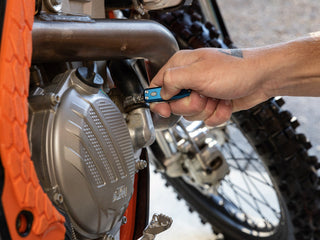 A man using his Elko EDC keychain slip joint folding pocket knife to fix a motorcycle.
