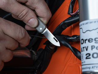 A man using his Elko EDC keychain slip joint folding pocket knife to repair fuel lines on a motorcycle.