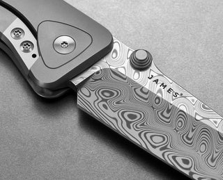 The blade of The Barnes integral titanium EDC frame lock pocket knife with Damasteel blade and black Micarta handle.