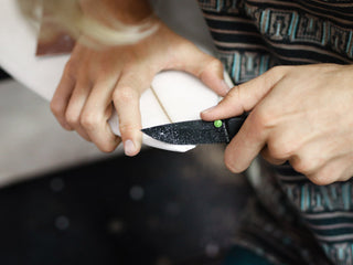 A man using his EDC folding pocket knife when shaping a surfboard.