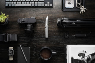 The Chapter 2 EDC frame lock titanium folding pocket knife open on a desk with other accessories.