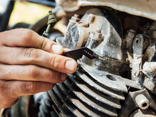A man using his The Halifax EDC keychain multitool scrape mud off of his dirt bike.