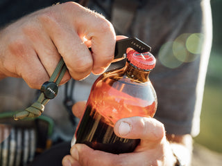 A man opening a bottle of beer with his Halifax EDC keychain multitool.