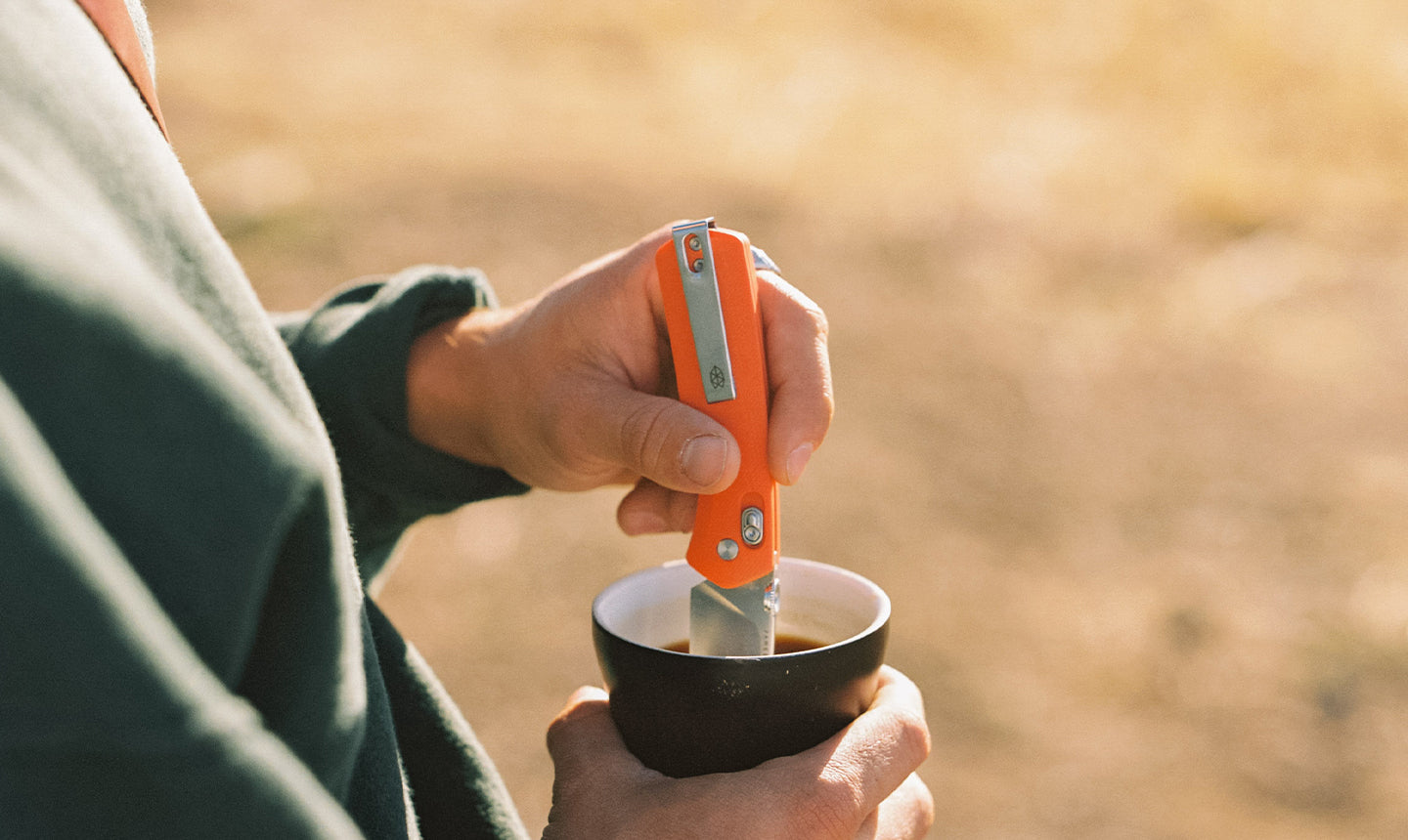 A man using his Carter folding pocket knife to stir his coffee.