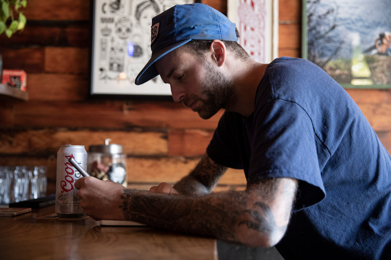 A man sitting at the bar, writing in his notebook with a Stilwell compact pen.