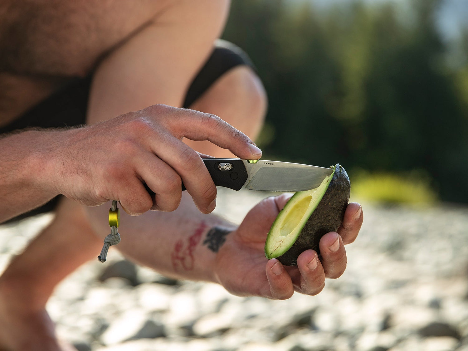 A man slicing an avocado with his Carter EDC slide lock folding pocket knife by a river.