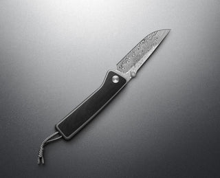 The Barnes integral titanium EDC frame lock pocket knife with Damasteel blade and black Micarta handle on a steel surface.