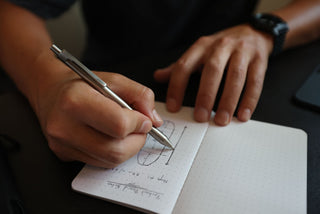 A man writing in a notebook with The Burwell EDC click pen.