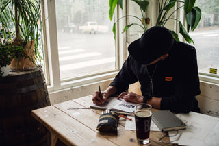 A man sketching in a notebook at a cafe with his Bolen titanium EDC twist pen.