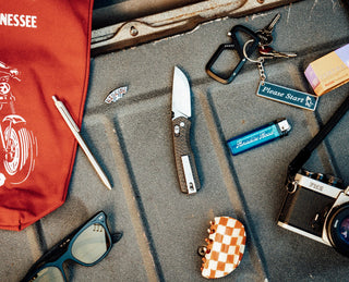 The Carter EDC slide lock folding pocket knife in carbon fiber on a truck bed with assorted gear.