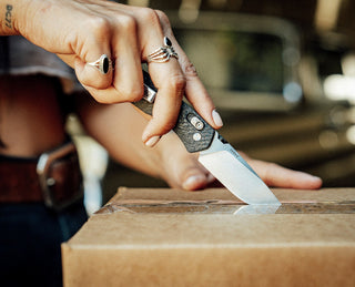 A women cutting a box with The Carter EDC slide lock folding pocket knife in carbon fiber.