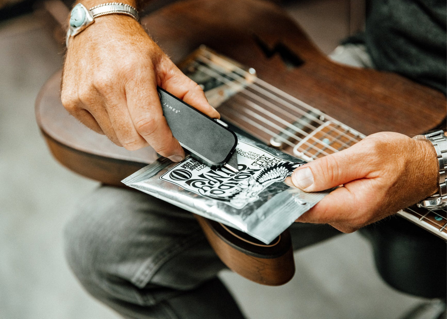 A musician opening a new set of guitar strings with a Palmer utility box cutter knife.